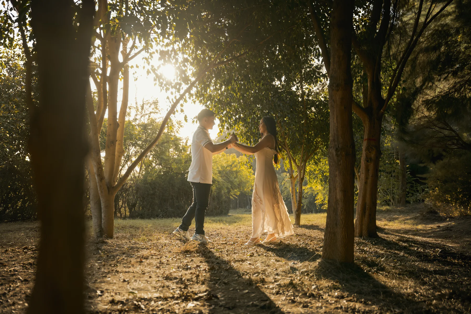 Pareja bailando entre árboles sobre un camino bañado por el sol