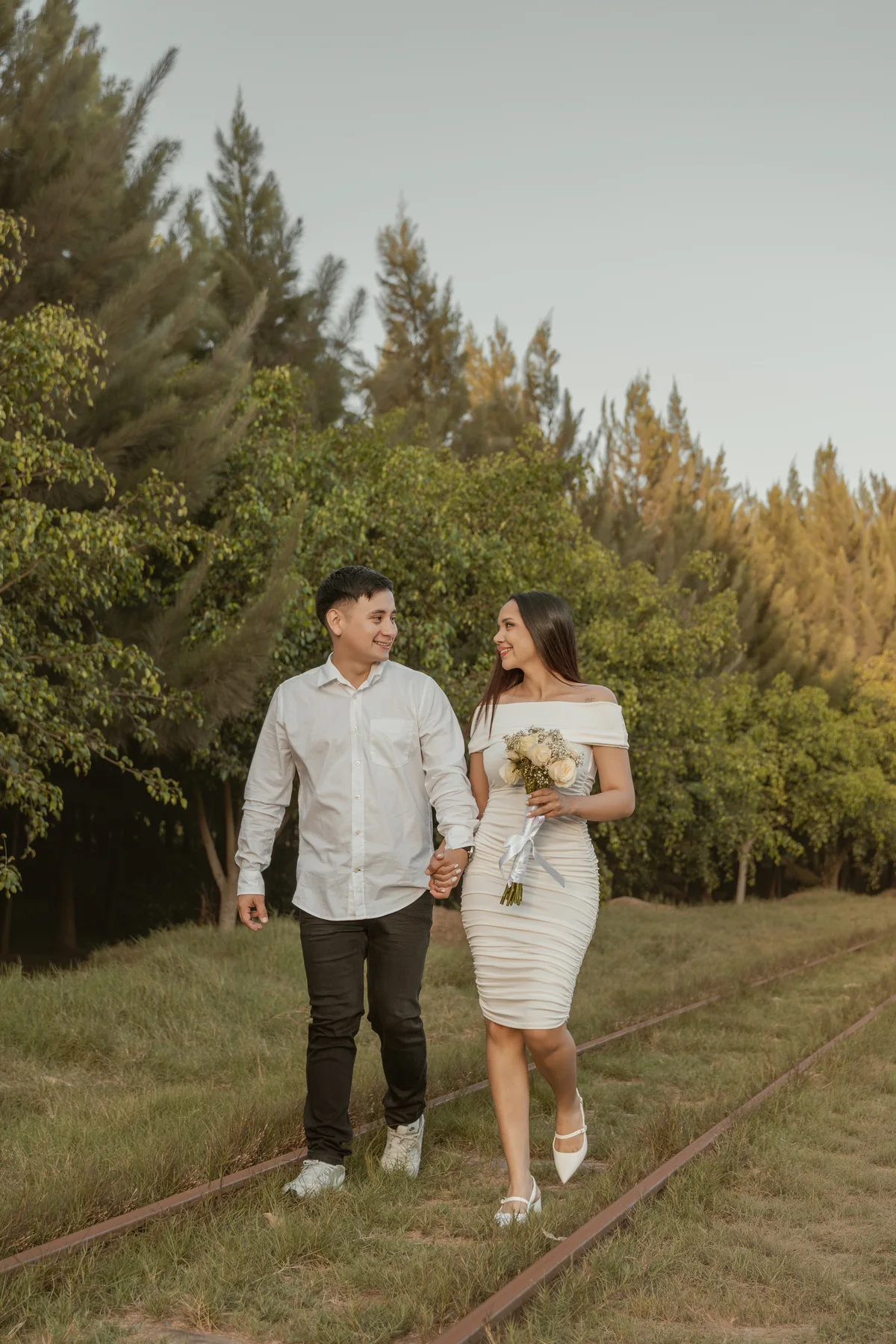 Pareja caminando de la mano por unas vías rodeadas de vegetación