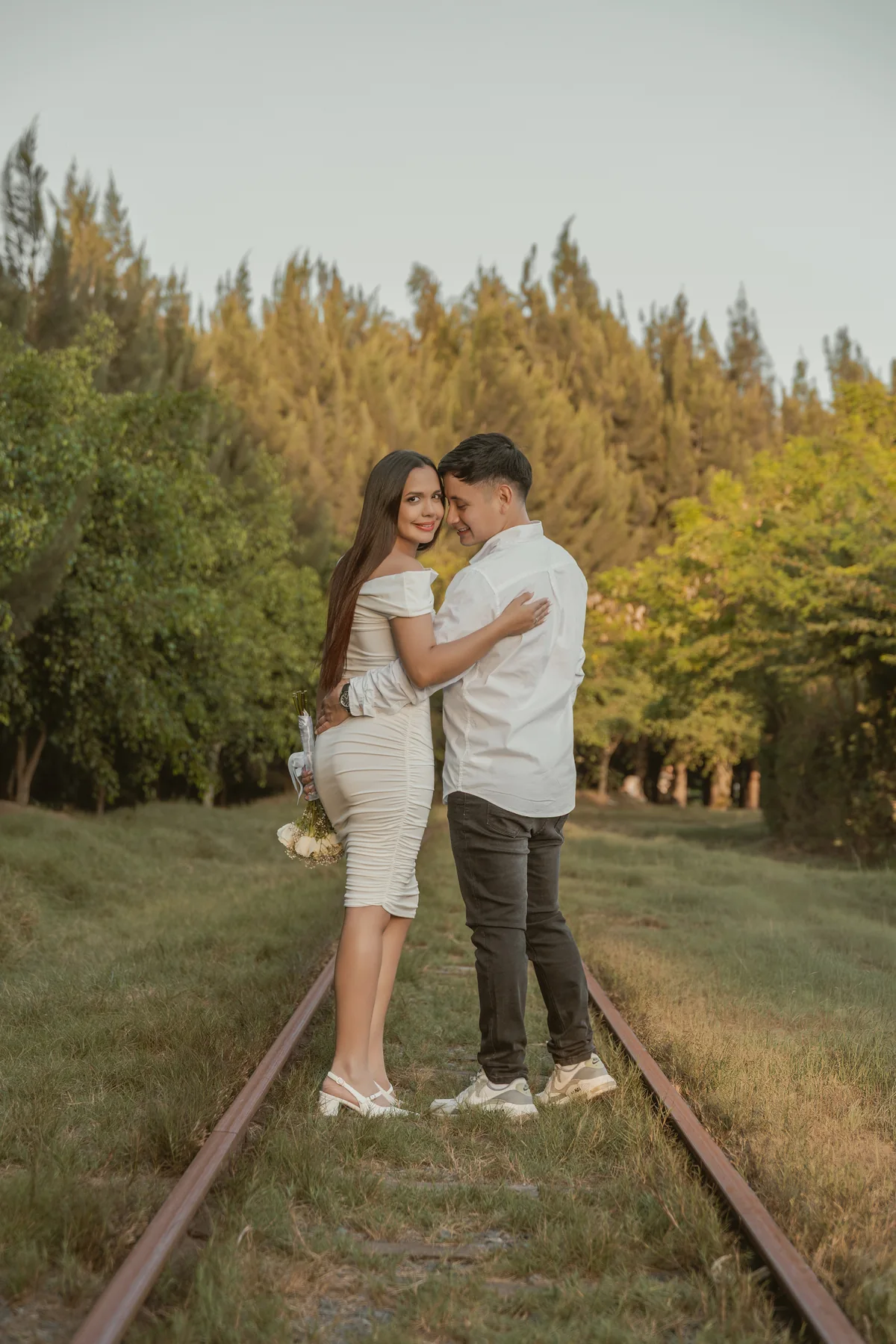 Pareja abrazada sobre las vías entre árboles y arbustos