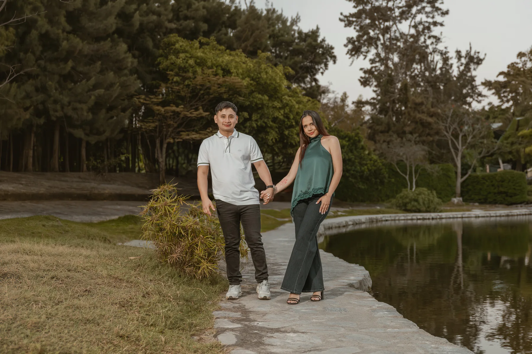 Pareja de la mano junto al agua con árboles y reflejos al fondo
